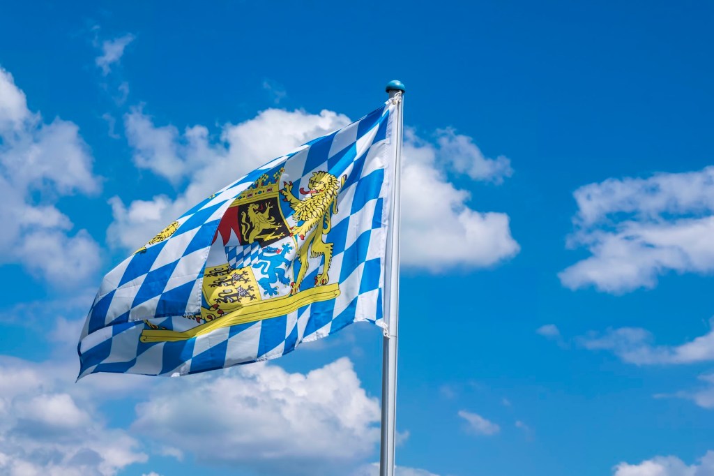The blue and white Bayern flag of Germany's Bavaria state, in front of a blue sky