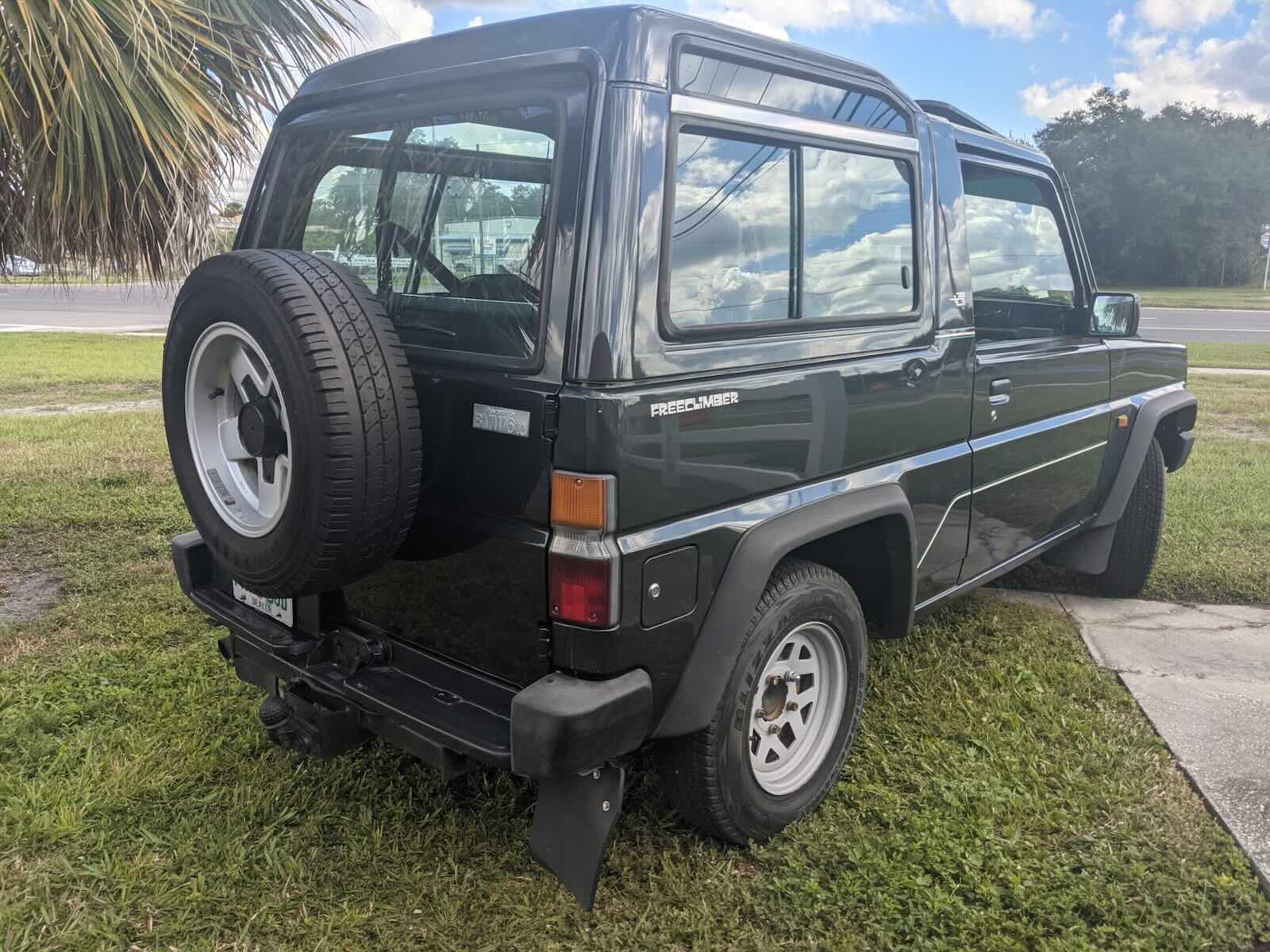 Rear of a Bertone Freeclimber two-door SUV parked on grass, palm trees visible in the background.