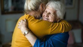 Young woman in a yellow shirt hugging an elderly woman wearing jewelry