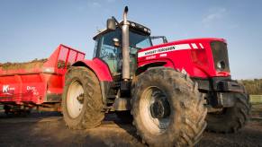 Red Massey Ferguson farm tractor pulling a trailer in a farmyard.