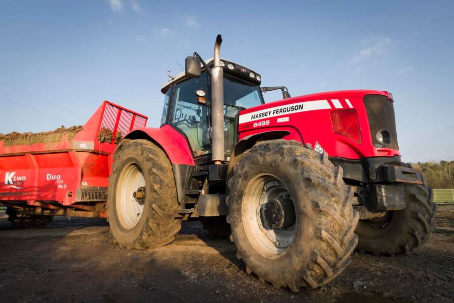 Red Massey Ferguson farm tractor pulling a trailer in a farmyard.