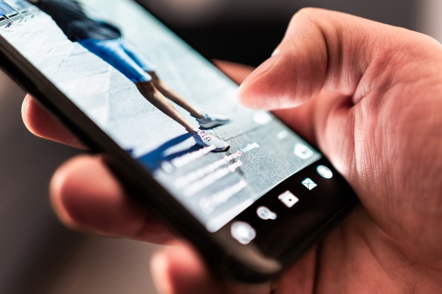 Police officer scrolling through TikTok while man is handcuffed in his police car on a hot day.