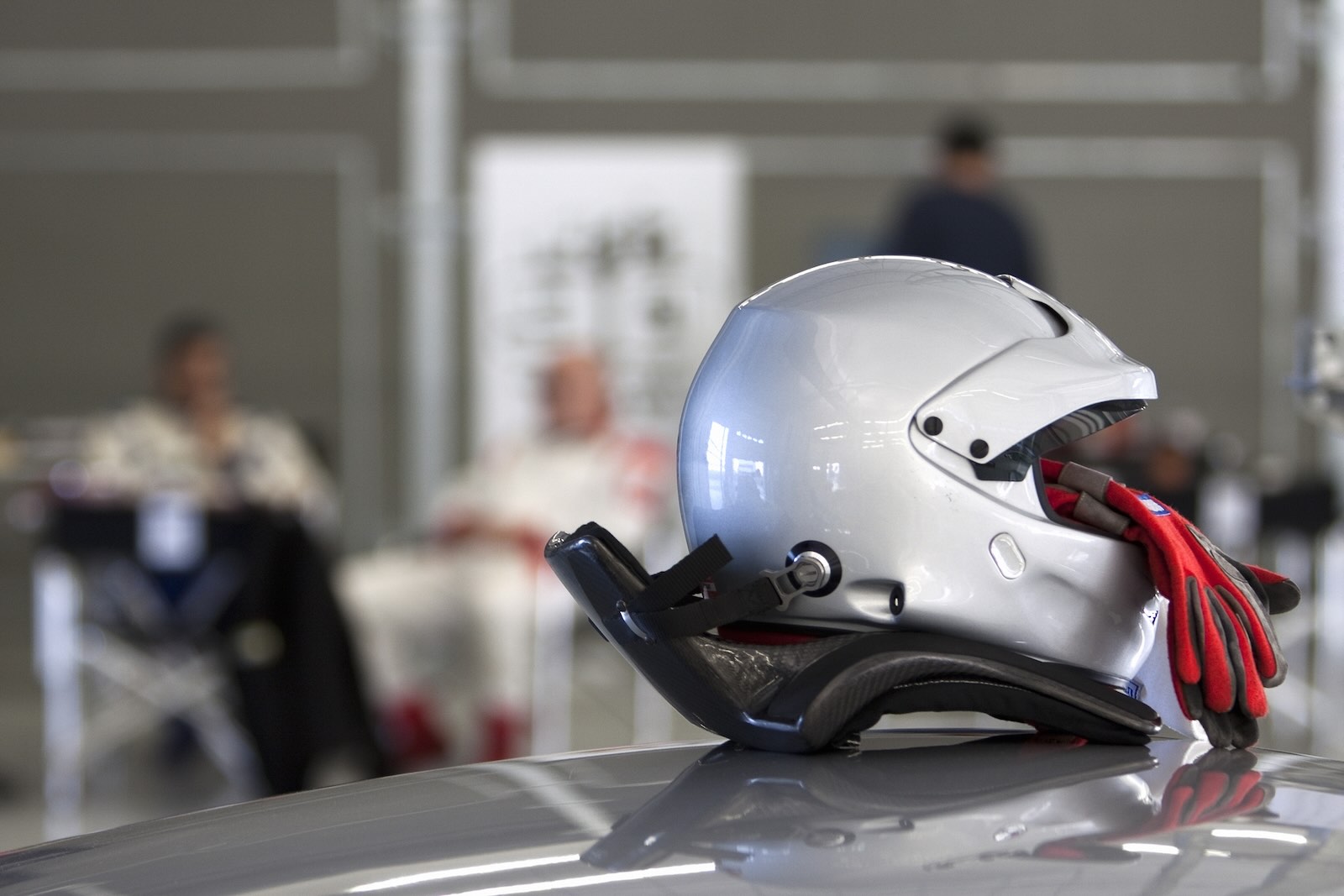 Silver racing helmet and red gloves on a car hood.