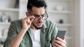 Car buyer squints at their phone and adjusts their glasses while reading a listing