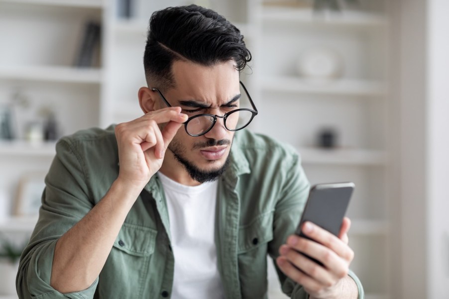 Car buyer squints at their phone and adjusts their glasses while reading a listing