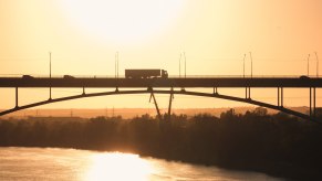 Semi truck silhouetted atop a bridge over a river