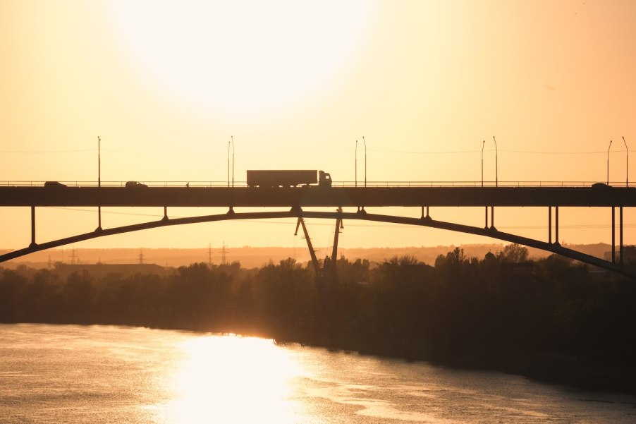 Semi truck silhouetted atop a bridge over a river