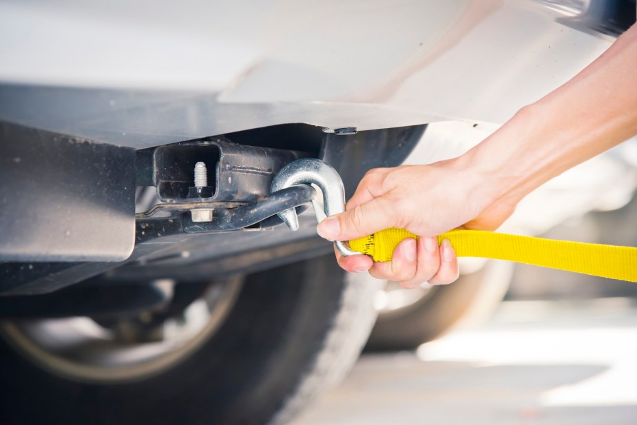 Hand attaching a tow hook to the bottom of a Mercury car.