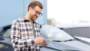 Toyota driver counts his cash from a class action lawsuit settlement, while standing in front of his car.