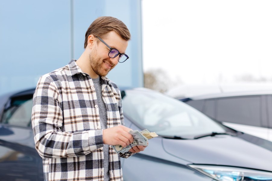 Toyota driver counts his cash from a class action lawsuit settlement, while standing in front of his car.