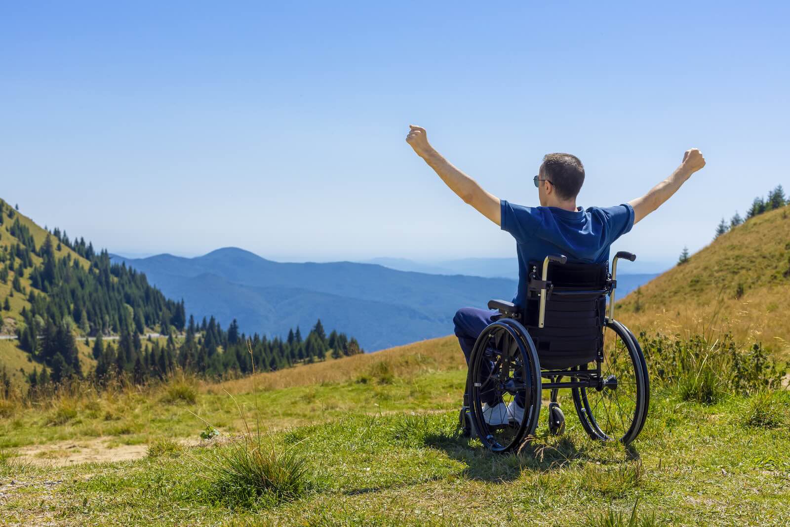 Wheelchair-bound main raises his arms in triumph on the top of a mountain in Wales.