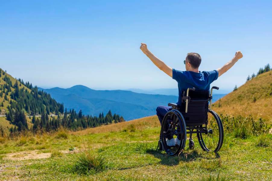 Wheelchair-bound main raises his arms in triumph on the top of a mountain in Wales.