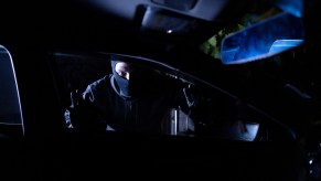 A car thief dressed in black and black mask looks into car window
