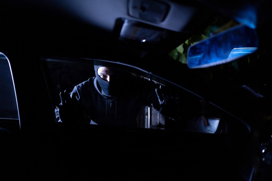 A car thief dressed in black and black mask looks into car window