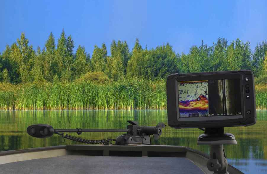 A boat on a water with lush greenery in background and close view of fishing sonar tool in foreground