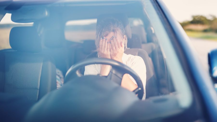 A frustrated female driver covering her face in direct front view of broken down car