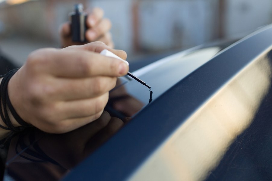 A man's hands putting touch-up paint on a car roofline