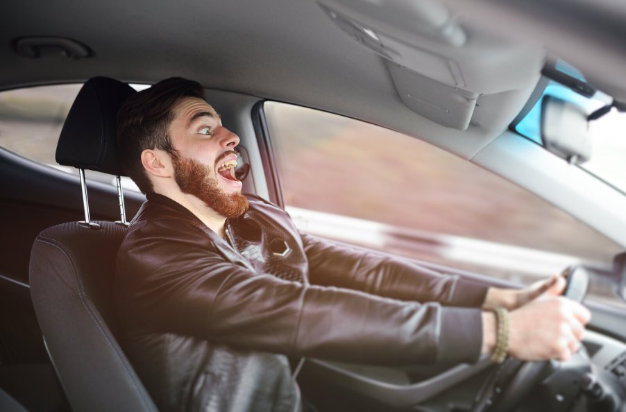 A male driver going fast with a crazed expression on his face, depicting abusing a rental car contract