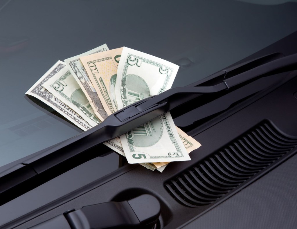 Wad of US currency bills under a car's windshield wiper.