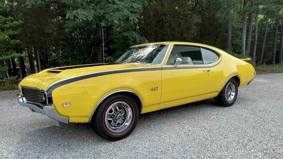A yellow 1969 Oldsmobile 442 parked on gravel in left front angle view