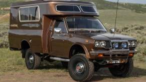 Vintage brown Toyota pickup truck with camper conversion parked in front of a mountain
