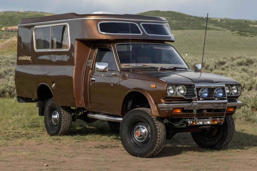 Vintage brown Toyota pickup truck with camper conversion parked in front of a mountain