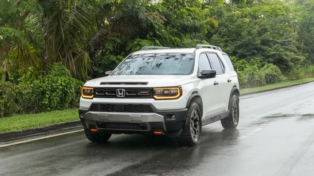 White Honda Passport drives down a paved road, palm trees visible in the background.