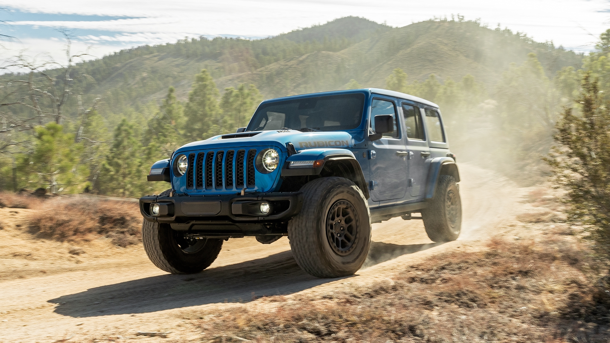 A blue 2022 Jeep Wrangler Rubicon on a dusty dirt road in low left front angle view