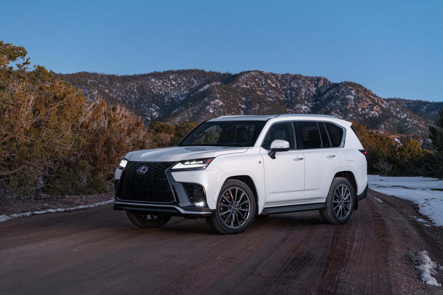 A white 2022 Lexus LX 600 parked in front of bare mountains at dusk in left front angle view