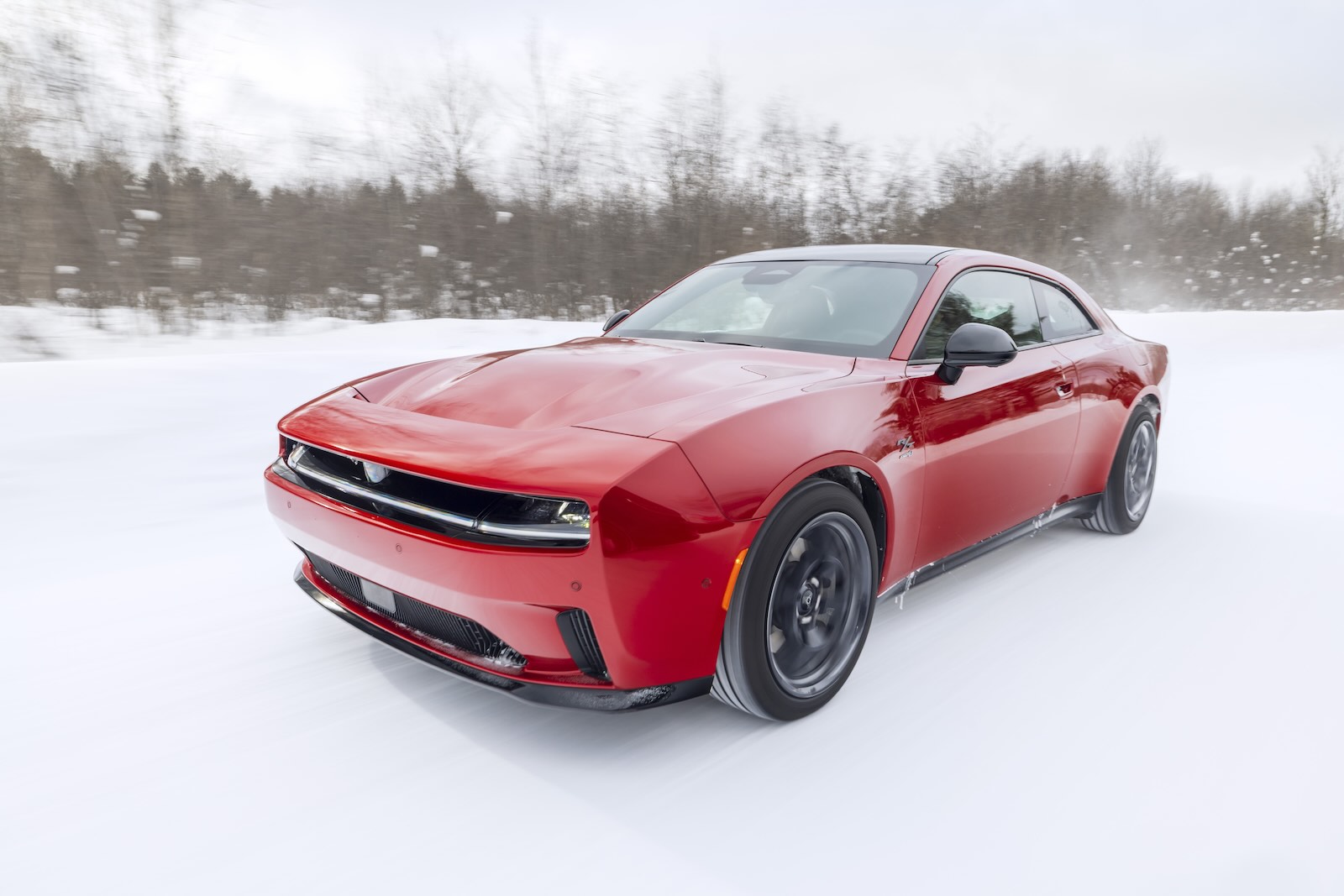 Red Dodge Charger EV driving through the snow, trees visible in the background.