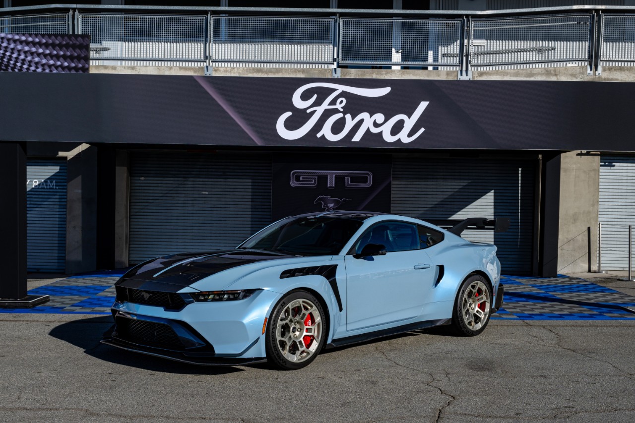 A blue 2025 Ford Mustang GTD parked in left front angle view under a Ford branded awning