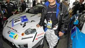 Toyota Chairman Akio Toyoda stands in front of a Lexus race car in the pits.