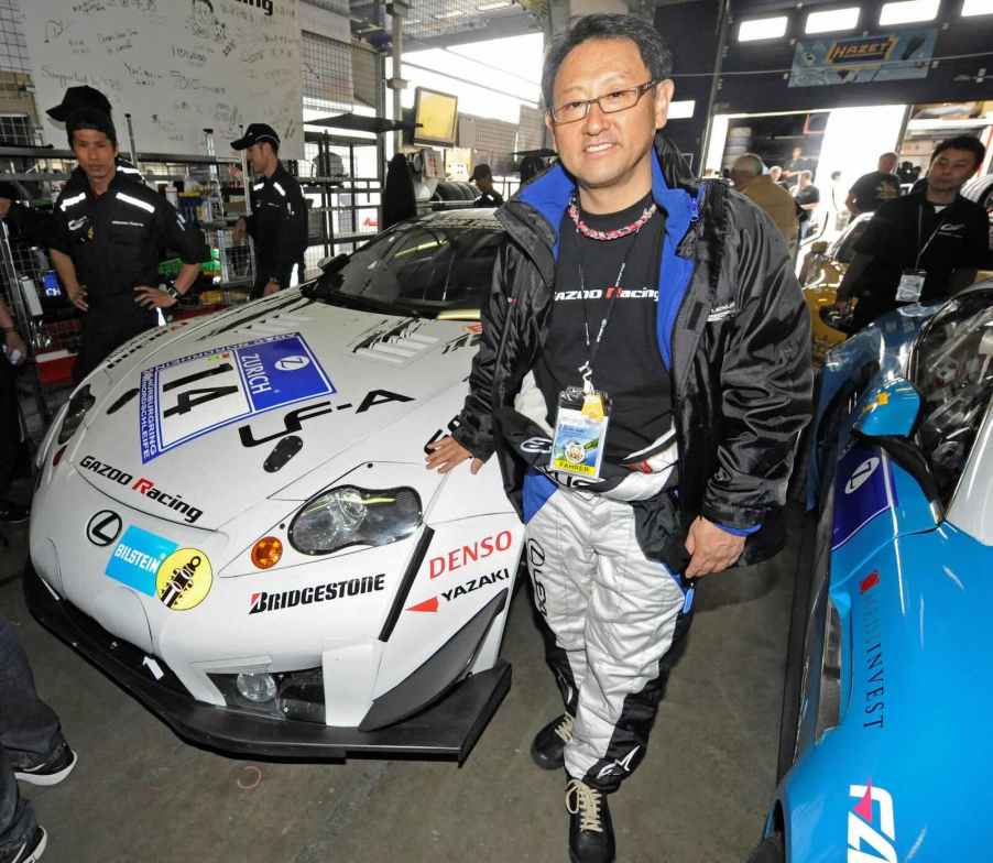 Toyota Chairman Akio Toyoda stands in front of a Lexus race car in the pits.