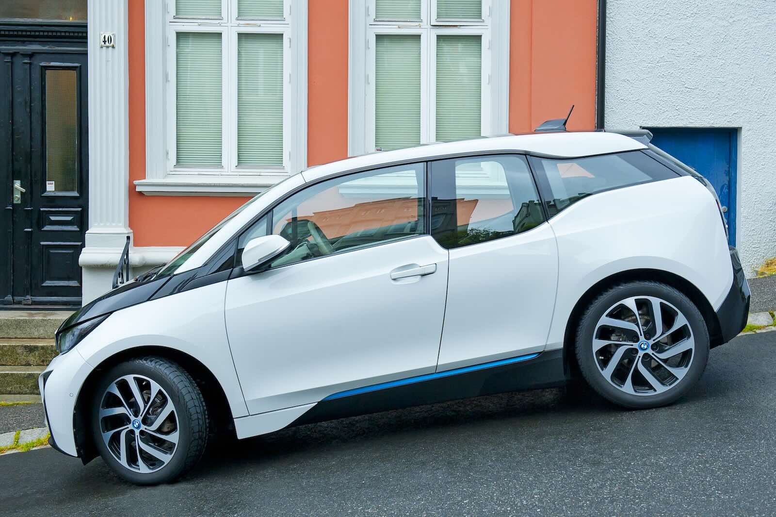 White BMW i3 range-extended hybrid EV parked on a hill in front of  an orange building