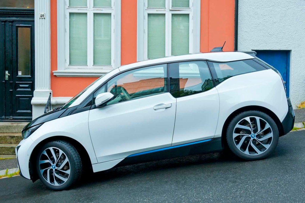 White BMW i3 range-extended hybrid EV parked on a hill in front of an orange building