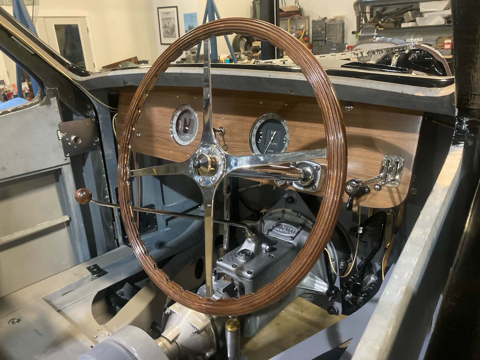 Steering wheel of a vintage Bugatti grand touring car undergoing restoration, a garage visible in the background.