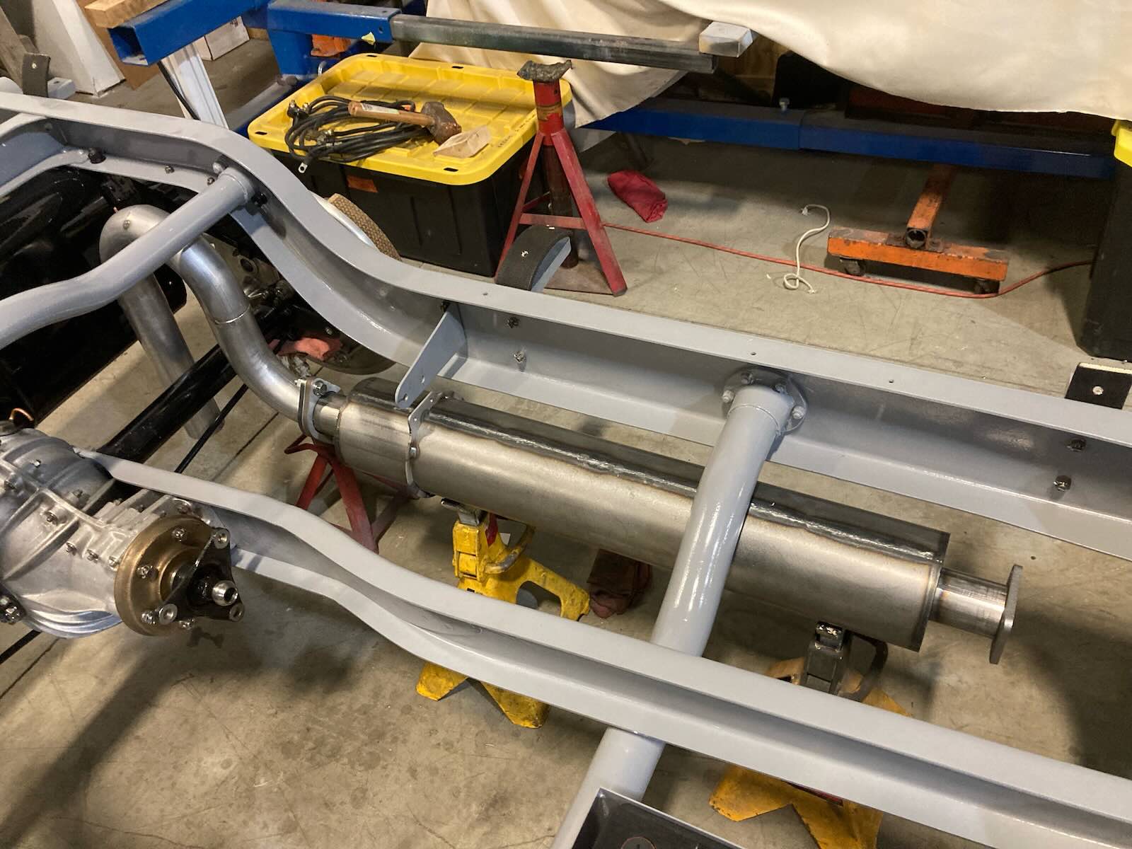 Frame of a vintage Bugatti grand touring car undergoing restoration, a garage visible in the background.