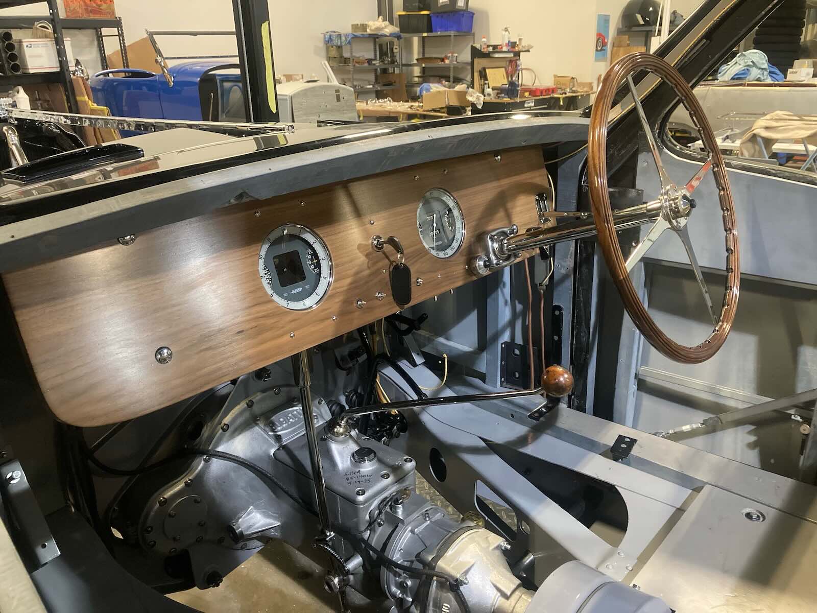 Steering wheel of a vintage Bugatti grand touring car undergoing restoration, a garage visible in the background.