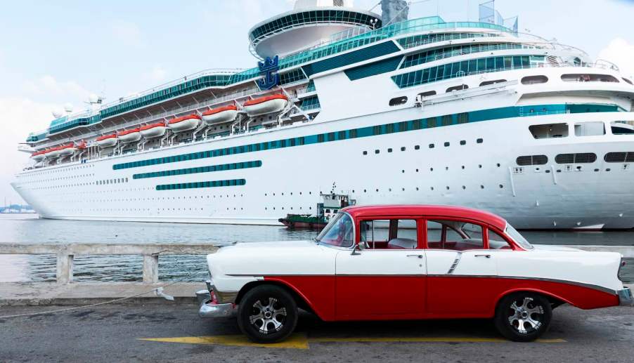 Classic red and white Chevrolet Belair parked in longterm port lot, a cruise ship visible in the background.