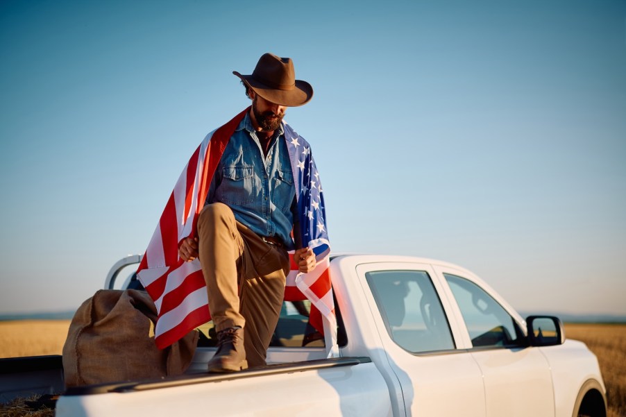 Cowboy holding an American flag stands in the back of a pickup truck