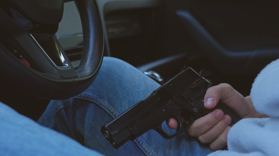 A man holding a handgun in the driver's seat of his car