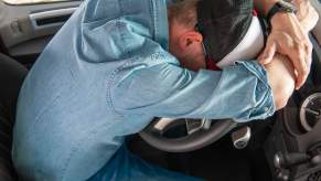 Florida man in denim and a hat sleeps slumped over the steering wheel of a stranger's car