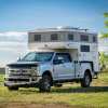 Super Duty Ford pickup truck with in-bed camper on a trip in the country, trees in the background.