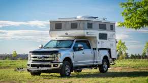Super Duty Ford pickup truck with in-bed camper on a trip in the country, trees in the background.