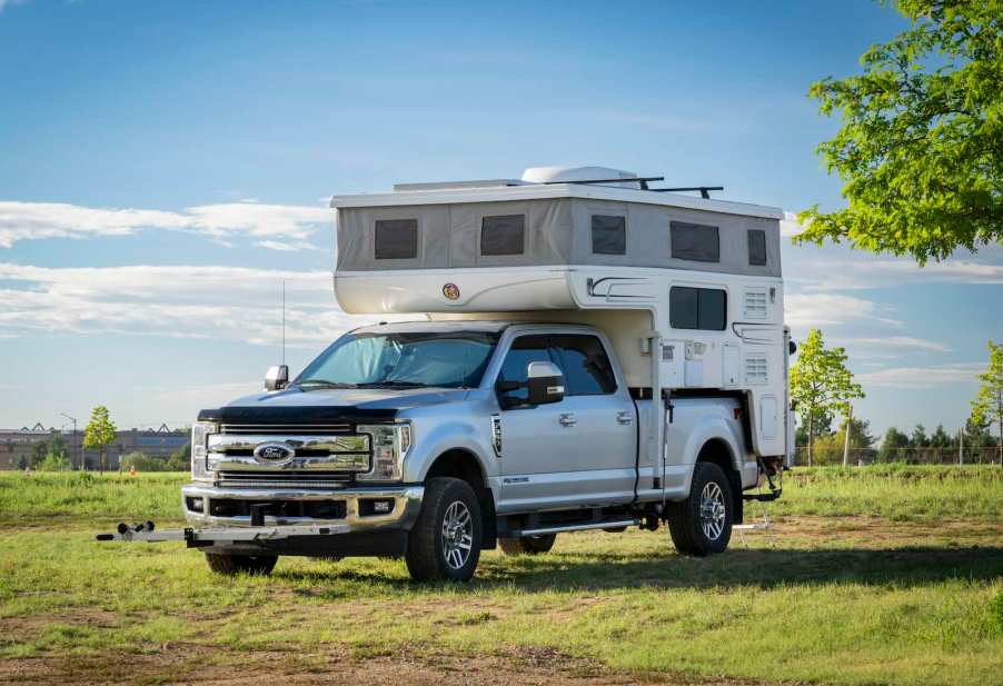 Super Duty Ford pickup truck with in-bed camper on a trip in the country, trees in the background.