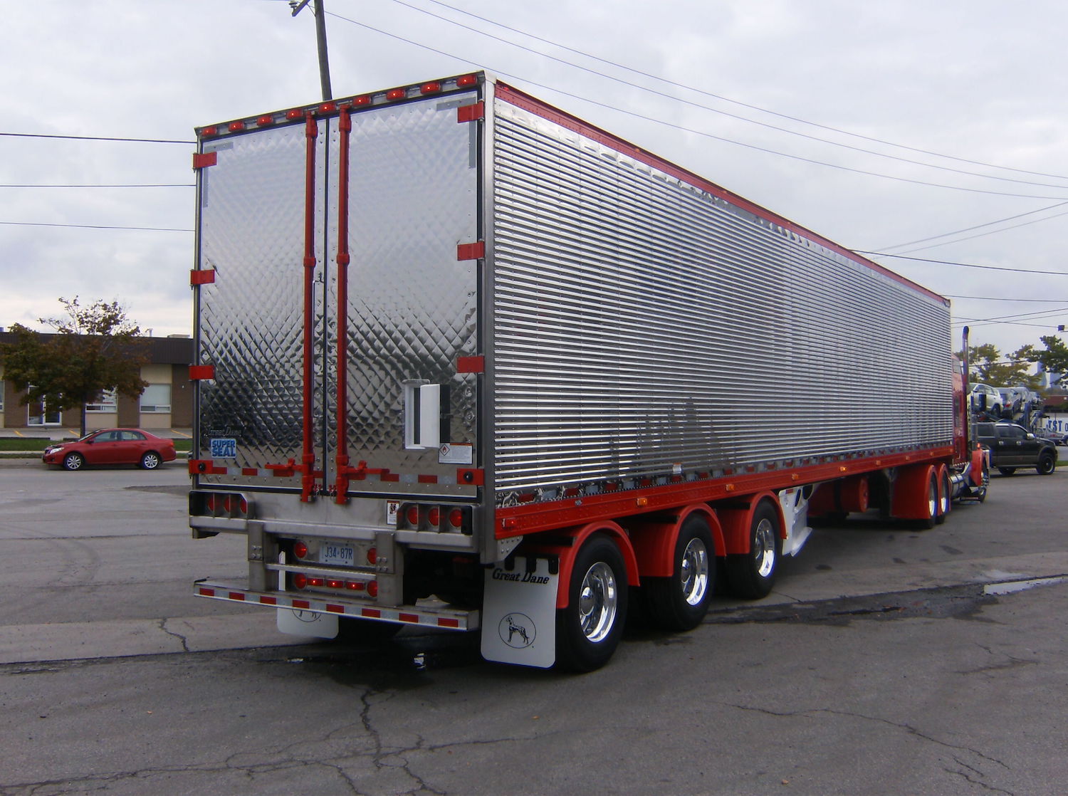 Chrome reefer semi truck trailer with a quilted rear door and a tiny ventilation door set into its main door, open.