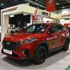 Red Hyundai Tucson N Line crossover SUV at an auto show, a display in the background.