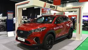 Red Hyundai Tucson N Line crossover SUV at an auto show, a display in the background.