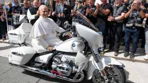 Pope Leo XIV sits on a BMW cruiser motorcycle, while the Jesus Bikers club stands behind him and cheers.