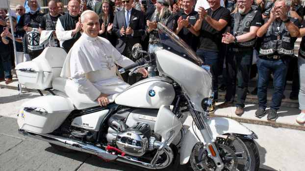 Pope Leo XIV sits on a BMW cruiser motorcycle, while the Jesus Bikers club stands behind him and cheers.